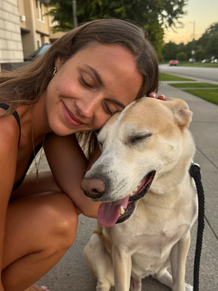 Woman resting her forehead against her calm dog at golden hour