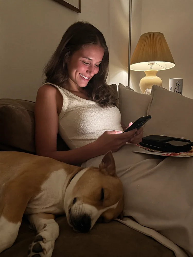 Woman on the couch at night with her sleeping dog, looking at the app